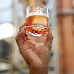 Hand holding glass with amber liquid and ice, "Delta Dirt" logo visible