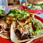 Close-up of a taco with shredded pork, slaw, and cilantro.